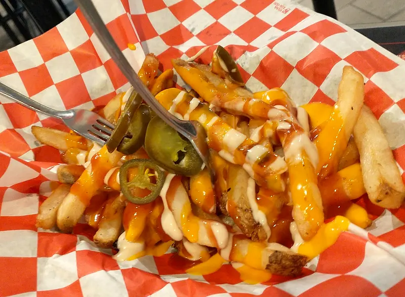 Papas tradicionales con queso amarillo, catsup, mayonesa y jalapeño sobre papel de cuadros rojos